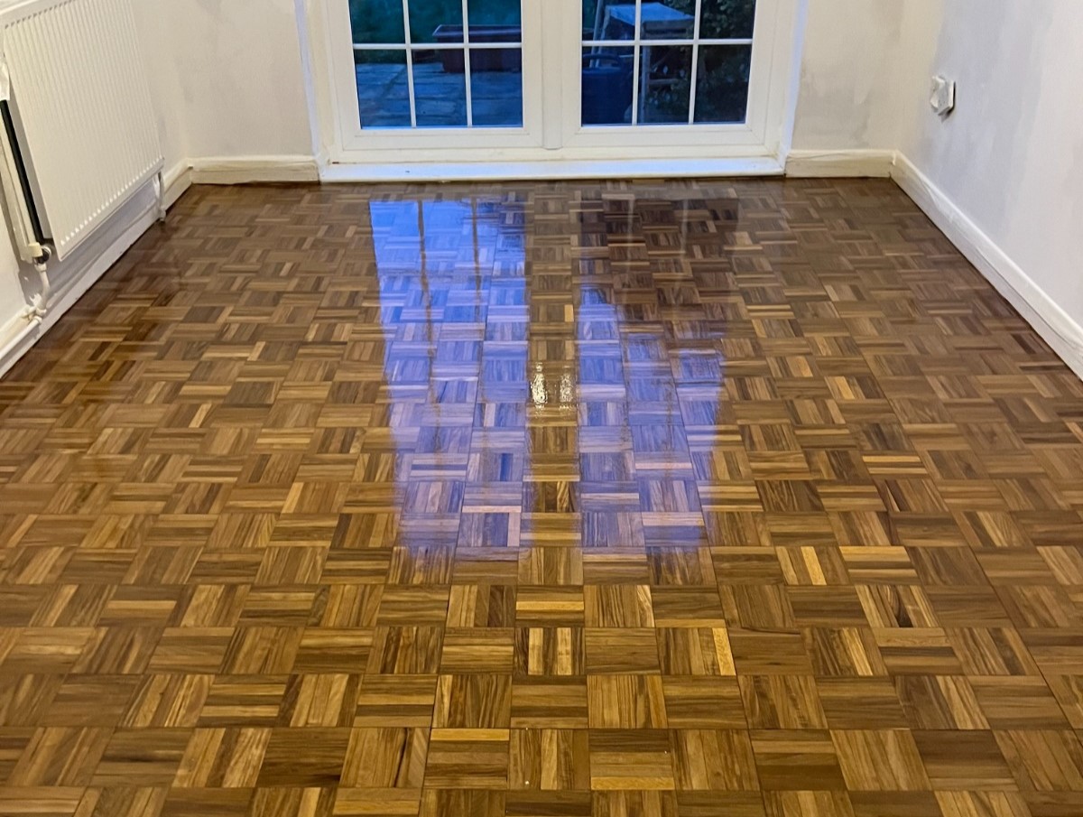 Completed wood floor sanding on an oak finger block parquet floor with a high-gloss reflective finish.