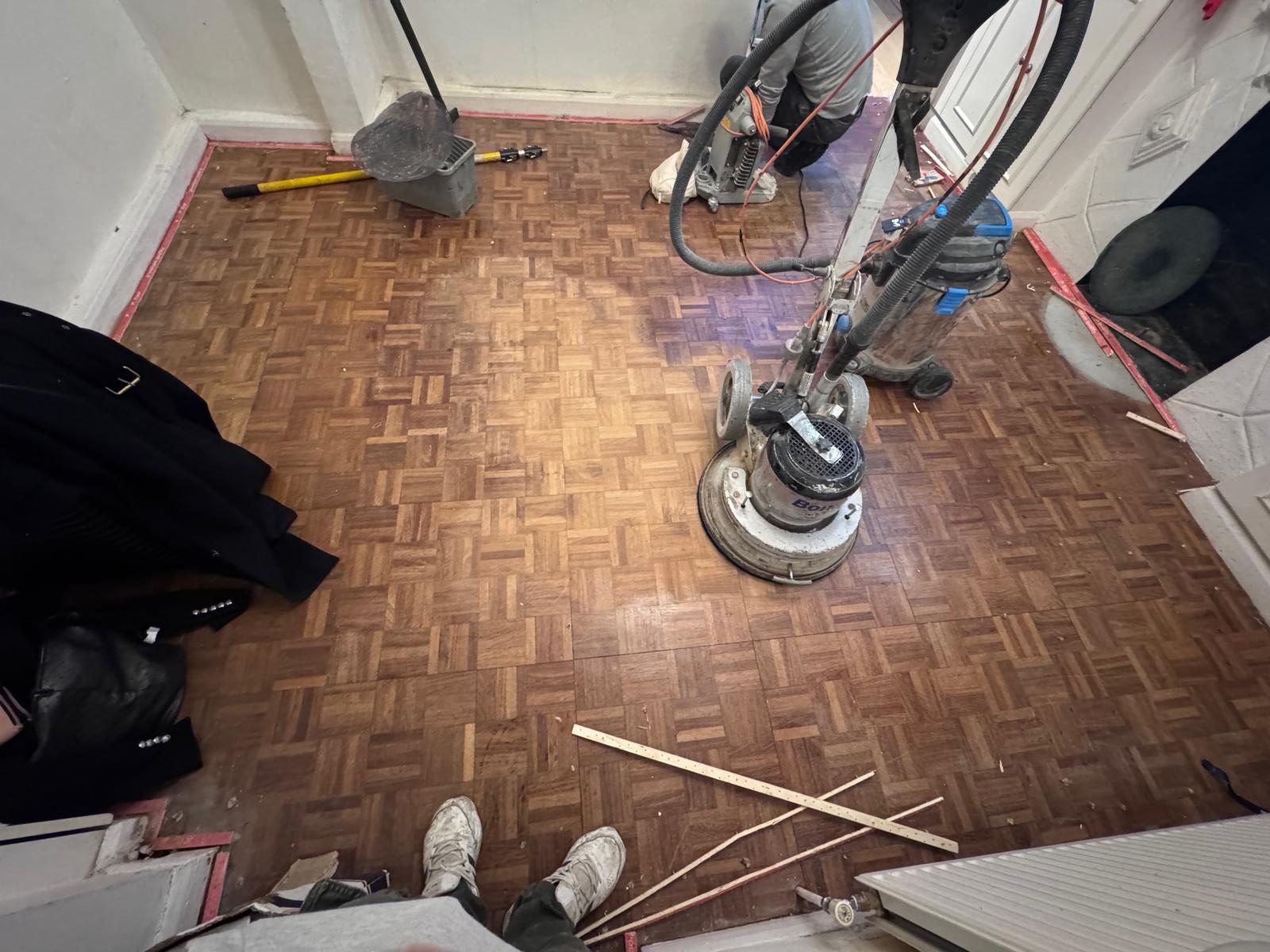 Professional wood floor sanding of a mosaic oak parquet floor in a residential room using industrial sanding machinery.