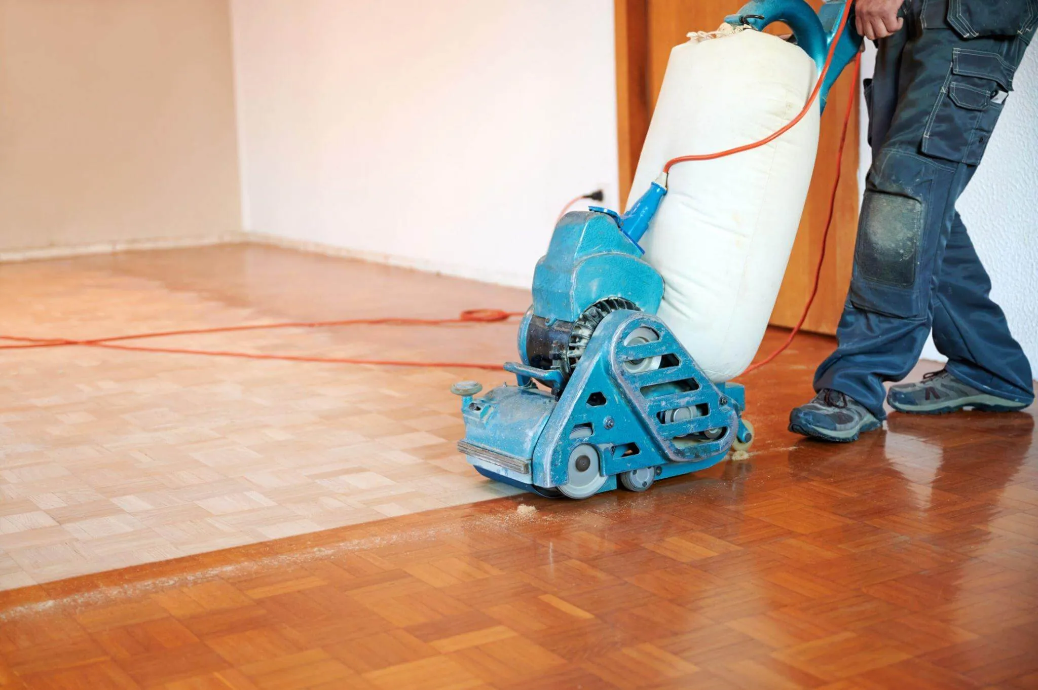 A professional contractor using a heavy-duty belt sander for wood floor sanding on an oak parquet floor.