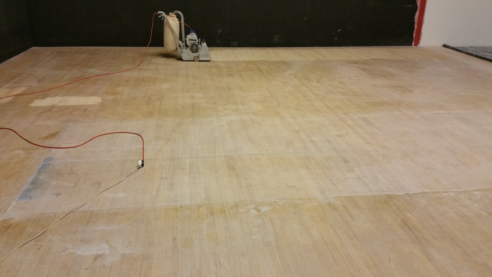 Commercial Floor Sanding in Carshalton on a maple hardwood sports hall floor, mid-preparation with sanding machine and cables on the bare boards.
