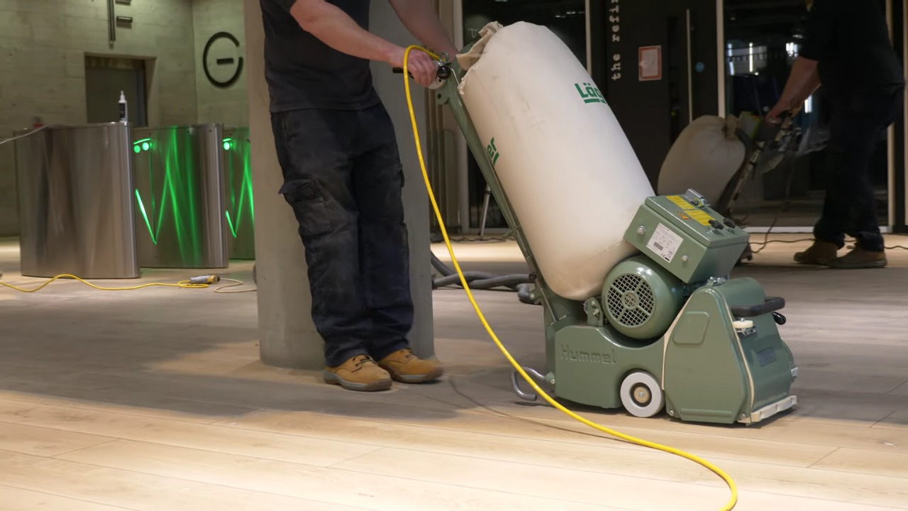 Commercial Floor Sanding in Carshalton on a light oak engineered plank lobby floor with a professional dust-free belt sander in use.